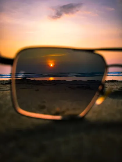 Reflecting on a beautiful sunset. This photo captures the setting sun reflected in a pair of sunglasses on the sand, offering a unique and personal view of a classic beach scene.