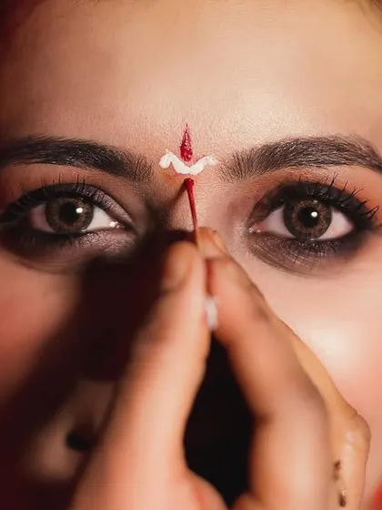 A detailed macro shot focusing on the makeup artist applying the traditional bindi to the bride's forehead. The intensity in her eyes makes this a powerful and intimate getting-ready photo.