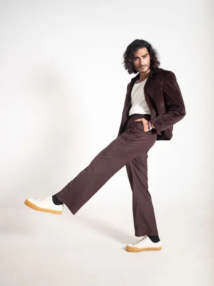 A playful studio shot of Vishak Nair in a brown velvet suit paired with casual sneakers. This demonstrates how to dress down a suit for a more modern, relaxed feel.