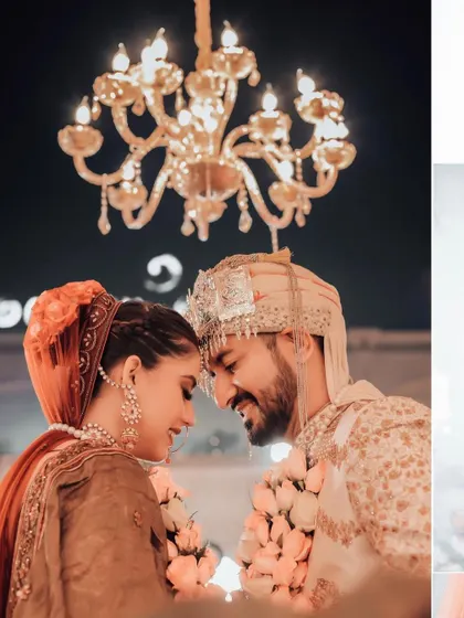 An intimate close-up of the couple, their foreheads touching. The warm glow of the chandelier above them adds a romantic and dreamy quality to this wedding portrait.