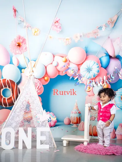 A personalized touch for Rutvik's first birthday! The custom name on the backdrop makes the celebration even more special, surrounded by a whimsical world of donuts and balloons.