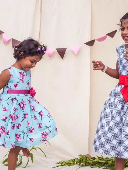 A playful moment between two friends. This image features a bright floral dress and a classic checkered dress, both perfect for a day of fun.