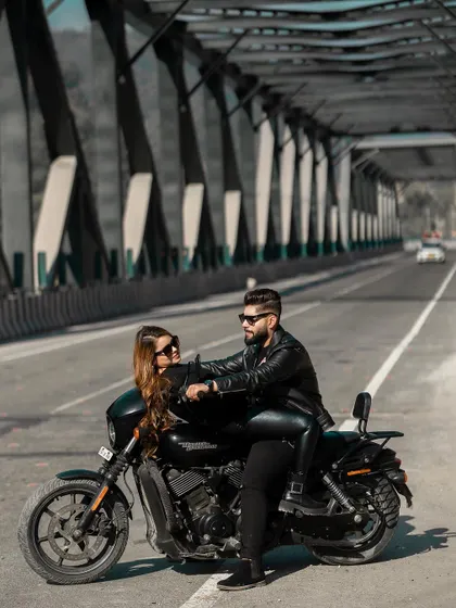 For the modern, adventurous couple, a pre-wedding shoot with an edge. This shot captures a cool, confident pose on a Harley Davidson against the industrial backdrop of a bridge, telling a story of love and shared passions.