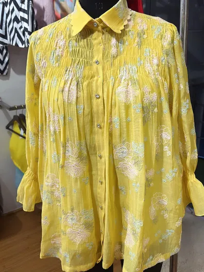 Perfect for a brunch outing, this yellow Chanderi shirt features beautiful floral embroidery and a smocked yoke. The scalloped collar and delicate buttons add to its charm.