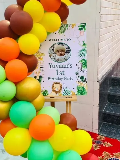 A personalized welcome sign for a jungle-themed first birthday party. The easel is decorated with a colorful balloon garland that matches the party's theme, greeting guests as they arrive.