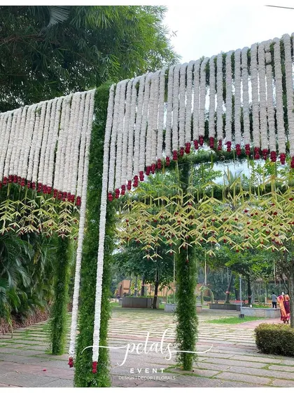 An entrance arch of white chrysanthemums, red roses, and green thoran, creating a look of captivating splendor.