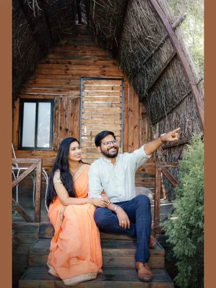 A candid moment on the porch of a rustic wooden cabin. The groom points towards their future, sharing a laugh with his bride-to-be in this natural and joyful pre-wedding photograph.