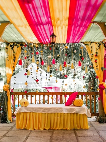 A colorful Mehendi setup with bright pink, yellow, and green drapes creating a festive canopy for the celebration.