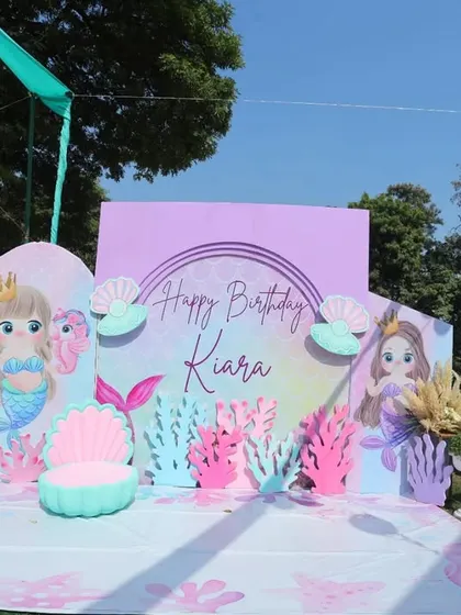 The main photo backdrop for Kiara's mermaid-themed birthday. The detailed and colorful setup makes for a perfect photo opportunity for the birthday girl and her guests.