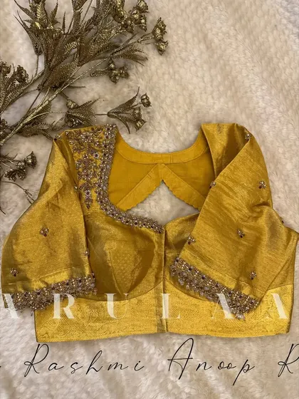 A mustard yellow blouse with a unique back cutout. The sleeves and neckline are adorned with heavy kundan and zardosi work for a rich, festive look.