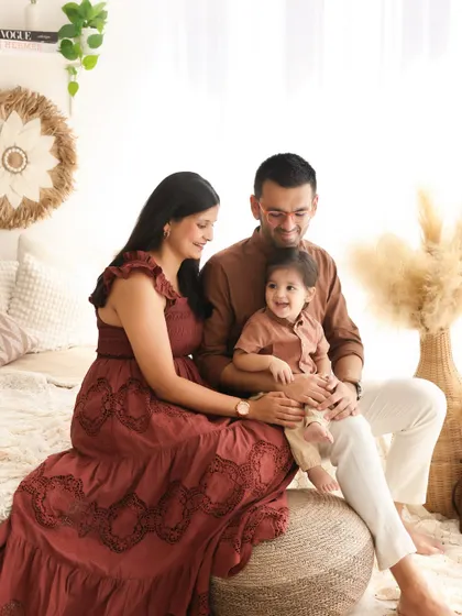 A warm and earthy family portrait. The coordinated brown and rust tones of their outfits blend beautifully with the boho decor, creating a cohesive and stylish look.