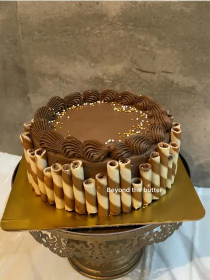 A simple yet elegant chocolate cake, decorated with chocolate wafer rolls around the side and delicate piping on top.