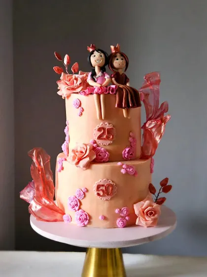 This beautiful two-tiered cake was for a joint birthday celebration for a mother and daughter. It features a peach and rose gold color scheme, handcrafted princess figurines, sugar roses, and delicate rice paper sails.