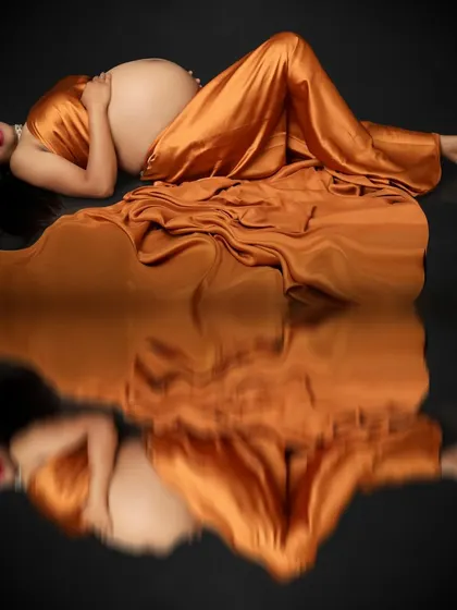 Embracing the pregnancy glow, this portrait captures the mom-to-be lying peacefully in a golden satin gown. The reflection on the floor doubles the beauty of this serene moment.