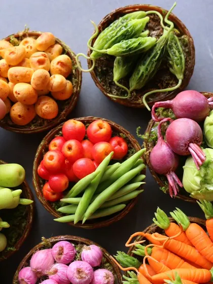 A collection of vegetable baskets, including potatoes, bitter gourd, beetroot, and carrots.