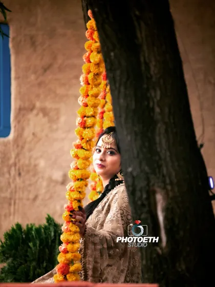 A beautiful solo portrait of the bride-to-be in traditional attire. The marigold garlands and rustic setting add a lovely ethnic touch.