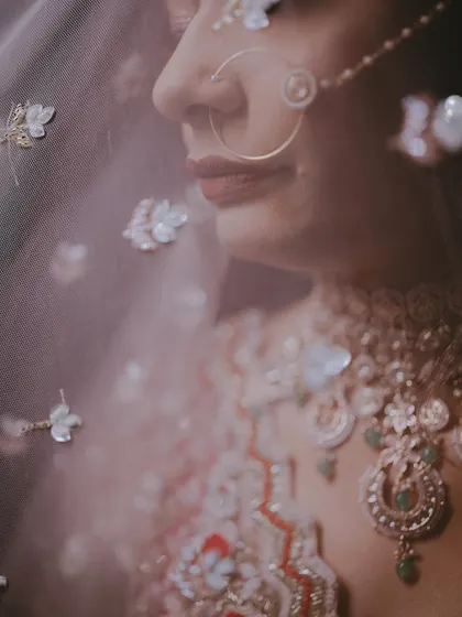 An artistic close-up through the veil, creating a soft, dreamy effect that highlights the bride's nose ring and the floral details on the fabric.