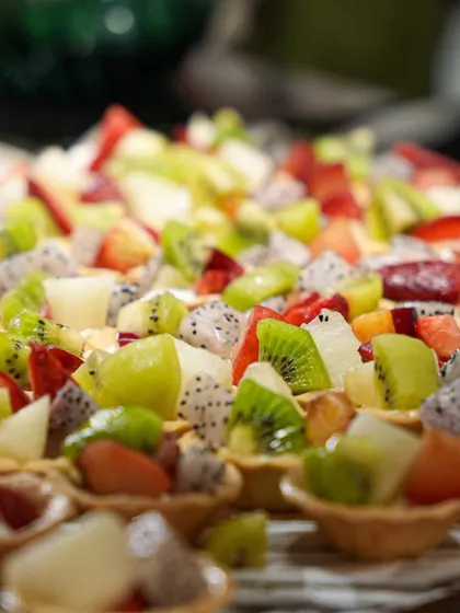 A close-up of our mini fruit tarts, topped with a colourful medley of kiwi, dragon fruit, and strawberries. These vibrant and refreshing bites are a healthy and beautiful dessert option.