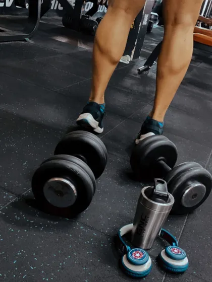 All progress takes place outside the comfort zone. This shot captures the essentials for a great leg day: heavy dumbbells for calf raises, headphones for focus, and a shaker for intra-workout fuel.