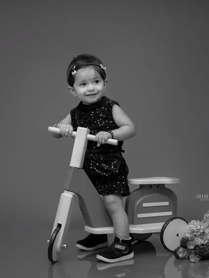A timeless black and white photo of a little girl on a toy scooter. This classic edit focuses on her expression and the clean lines of the composition.