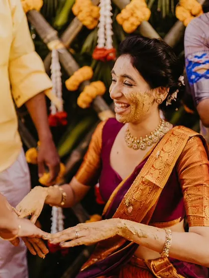 A candid moment from a Telugu Haldi ceremony, capturing the bride's joyous laughter against a traditional bamboo and marigold backdrop.