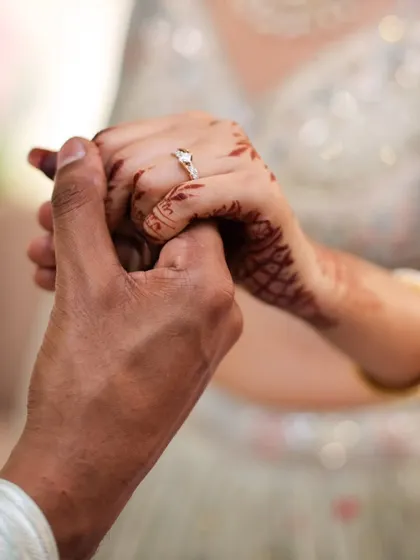 A close-up shot of an engaged couple holding hands, focusing on the bride's ring and henna.