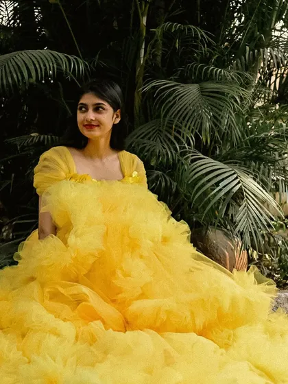 The yellow ruffle gown looks stunning against the lush green background.