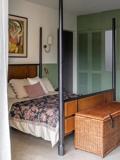 The primary bedroom in the Rio Home balances comfort with character. We used a punchy sage green for the wainscoting and wardrobe, paired with a four-poster bed and a vintage wicker trunk to create a space that feels like a personal refuge.