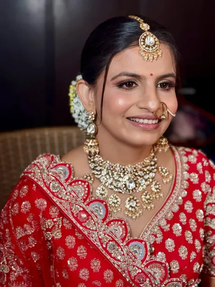 A smiling bride in a traditional red lehenga, her makeup is classic with a focus on flawless skin and defined eyes.