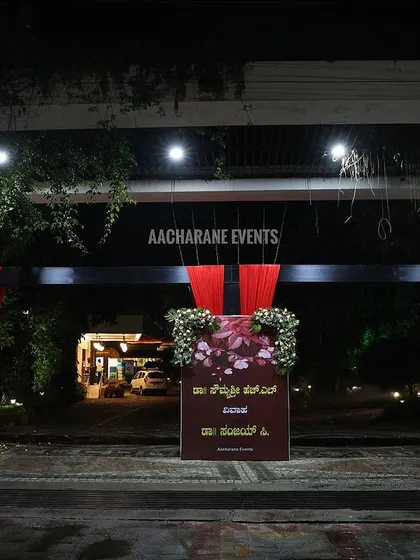 A simple yet elegant entrance arch for a night event in Hassan. The design uses deep red fabrics and floral accents, with signboards in Kannada to welcome the guests in a traditional way.