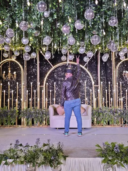 A glamorous Sangeet or reception stage with a sparkling black backdrop, art-deco arches, and a ceiling of hanging disco balls.