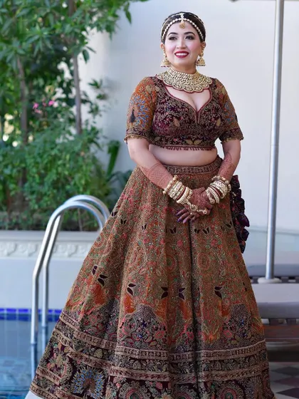 A full view of a royal bridal look. The hair is pulled back into a neat, traditional bun, allowing the magnificent 'matha patti' and lehenga to be the stars of the show.