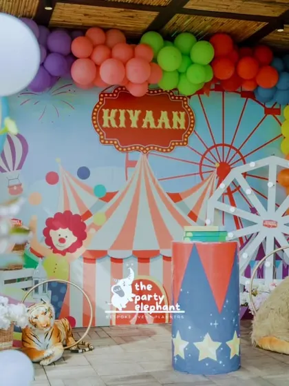 Step right up to a whimsical carnival birthday. This vibrant backdrop features a custom circus tent and ferris wheel design, framed by a colorful balloon garland and playful animal props, setting the stage for a day of fun and games.