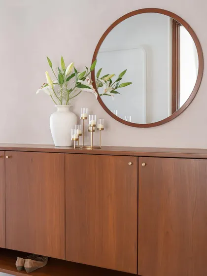 The foyer in 'Living life in colours' is a subtle prelude to the vibrant home inside. It features a teak shoe cabinet against a soft peach textured wall, creating a warm and muted entrance.