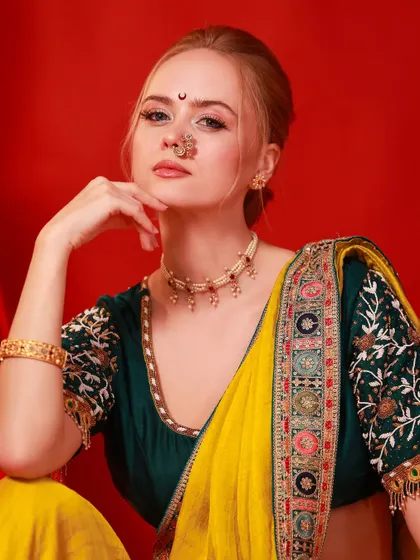A stunning festive portrait against a rich red background. The model's traditional attire, complete with a nath and bindi, is vibrant and captures a celebratory mood.