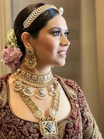 A real bride with a classic low bun, adorned with pink and white flowers. The hairstyle is complemented by a traditional matha patti, creating a regal bridal look.
