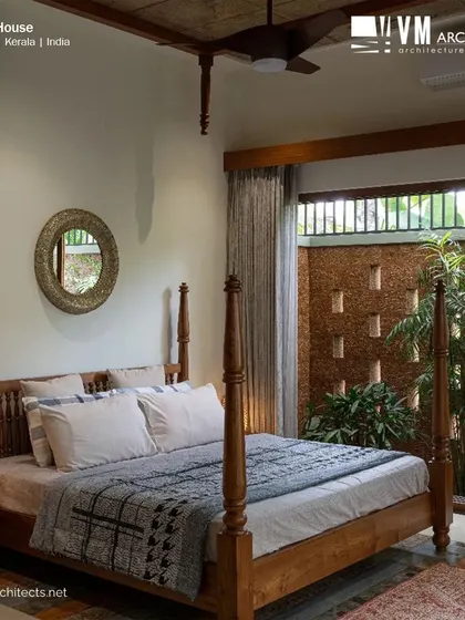 A traditional four-poster bed in Kuttiyil House, paired with a decorative mirror and an opening to a private courtyard with a perforated brick wall.