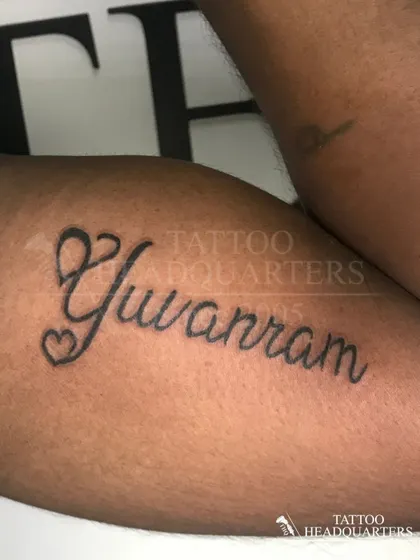 The name "Yuvram" in a flowing script with heart details, a beautiful and personal piece on the arm.