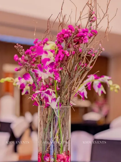 For a modern and artistic touch, we designed this floating floral arrangement. A tall glass vase holds magenta orchids and rustic twigs, creating a centerpiece with height, color, and texture for a chic Sangeet night.