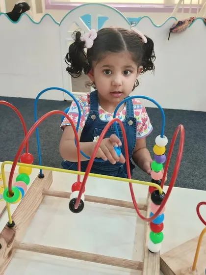 A young student explores a bead maze, a classic Montessori toy that develops fine motor skills, tracking, and concentration. Our environment is filled with tools for self-directed learning.