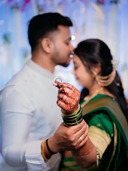The groom holds the bride's hand, showing off her engagement ring. This shot beautifully captures the detail of the ring and the henna on her hand, with the couple in a soft, romantic embrace.