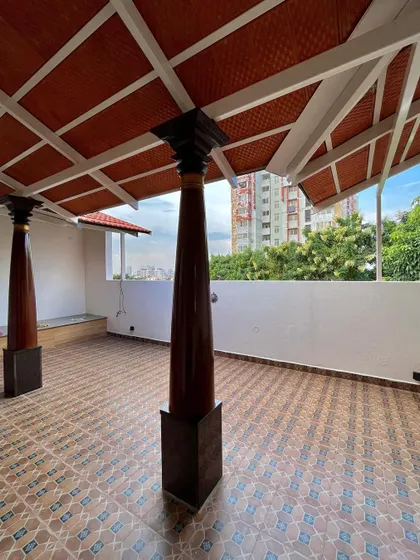 This terrace at Mr. Vinay's residence is designed as a semi-covered traditional sit-out. Featuring reclaimed wooden pillars and clay tile roofing, it offers a serene space with expansive city views.