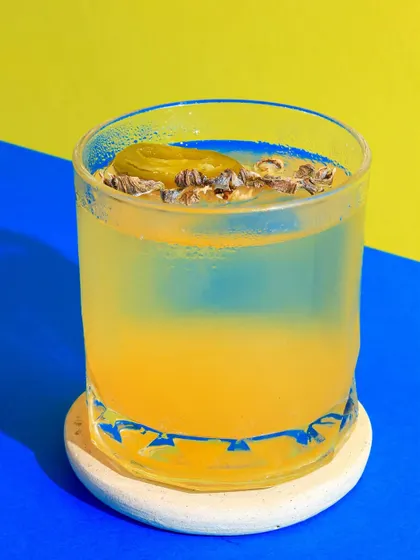 A unique yellow and blue cocktail with a pickled olive garnish, shot with bold colors to highlight its unusual ingredients.