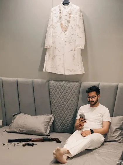 A candid, behind-the-scenes shot of the groom relaxing before the ceremony, with his sherwani hanging in the background, ready for the big moment.