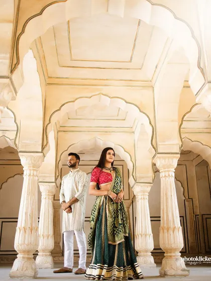 An elegant portrait of a couple standing between the majestic pillars and arches of a Jaipur palace, showcasing the grandeur of the location.