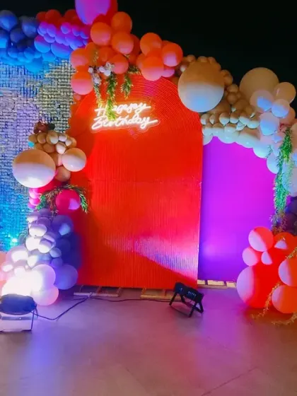 A bold and colorful rooftop party for a 35th birthday. The backdrop combines a red panel with a silver sequin wall, framed by a multi-colored balloon garland and large marquee numbers.