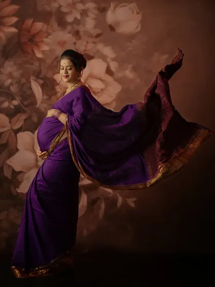 The flowing pallu of the purple saree adds a dynamic and artistic element to this beautiful solo maternity portrait in the studio.