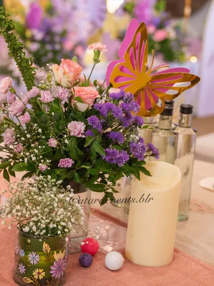 A closer look at a table centerpiece reveals a mix of fresh flowers, a golden butterfly, and a soft candle, creating a warm and enchanting atmosphere for guests.
