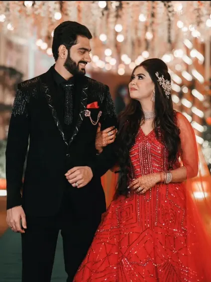 A perfect couple's look for a reception or engagement. The groom wears our custom black suit with unique silver embroidery on the shoulders and lapels, complementing his partner's vibrant red gown.