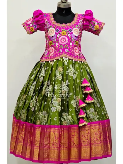 A grand-looking lehenga with a heavily embroidered pink blouse and a floral brocade skirt in olive green. The puff sleeves and latkans add a playful touch.